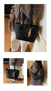 Close-up of black leather tote bag with elegant beaded charm and logo patch detail