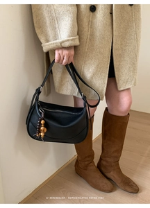 Detail of black leather shoulder bag featuring retro wooden beaded tassel and soft texture