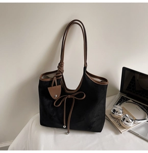 Close-up of black suede tote bag with brown trim, knotted handle, and bow detail