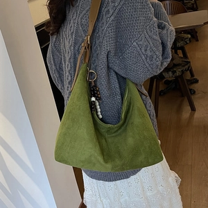 Close-up of green suede hobo bag with brown strap and decorative beaded charm detail