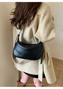 Black leather saddle bag shown on a model in a minimalist stylish indoor setting