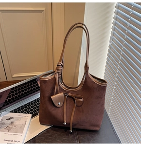 Close-up of brown suede tote bag with bow detail and heart charm under natural light