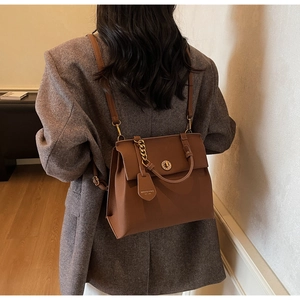 Vue détaillée du sac à main en cuir marron avec chaîne dorée sur un tailleur gris