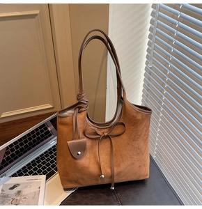 Detailed close-up of brown suede tote bag with bow detail and metal ball ornament