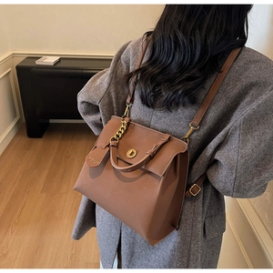 Détail du sac en cuir marron avec chaîne dorée et fermoir métallique sur manteau