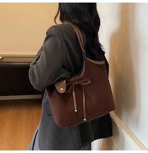 Detail of suede tote bag with bow accent and brown leather straps on model shoulder