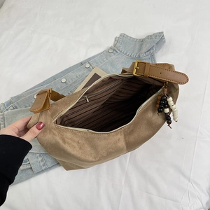 Detail of brown suede crossbody bag with retro gold hardware and bead tassel charm