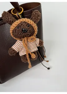 Close-up of a brown knitted bear keychain charm hanging on a premium leather handbag