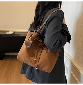 Detail of a brown suede tote bag with a bow accent and charm on a model's shoulder