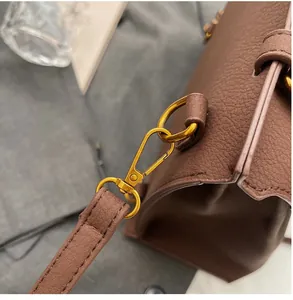 Détail rapproché des ferrures dorées et de la bandoulière en cuir marron du sac