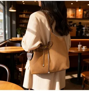 Brown suede tote bag with bow detail and matching small pouch shown in a cafe