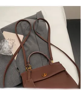 Détail du sac à main marron en cuir grainé avec fermoir doré sur une veste de costume