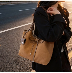 Close-up of brown suede tote bag with ribbon bow detail worn by a model in soft sunset light