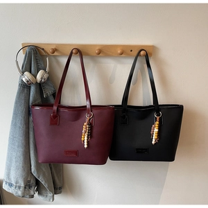 Close-up of matte PU leather tote bags with colorful wood bead charms on a wooden rack