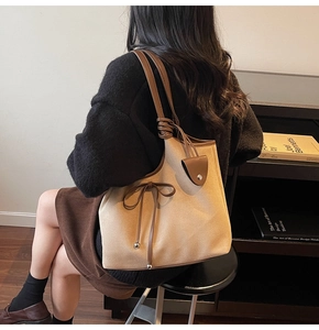 Detail of beige tote bag featuring a leather bow accent and brown strap on model