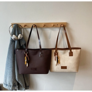Detail of minimalist tote bags with beaded charms and leather texture on a wooden rack