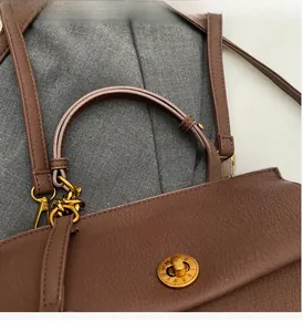 Détail d'un sac à main marron en cuir grainé avec fermoir romain doré et poignée chic