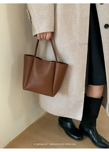 Detailed side view of a brown minimalist leather bucket bag held by a model in a beige coat