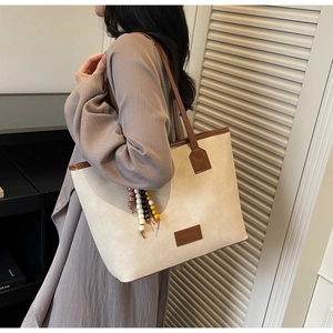 Close-up of beige tote bag with brown leather trim and a colorful beaded tassel charm