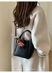 Detail of black pebbled leather tote bag with a cute bear charm on a beige coat