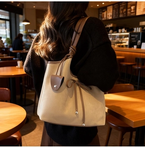Detail of a beige tote bag with a coffee brown shoulder strap and knotted bow detail