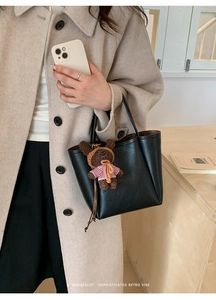 Chic black litchi grain tote bag with a cute plush bear charm in a lifestyle setting