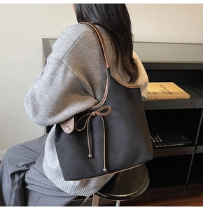 Close-up of minimalist black tote bag with brown bow detail worn over the shoulder