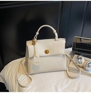 Détail d'un sac à main beige en cuir avec fermoir rotatif doré et pendentif chaîne