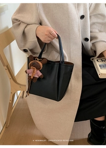 Detail of black pebbled leather bucket bag with cute brown teddy bear plush charm
