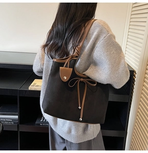 Detail of suede tote bag showing brown leather bow and shoulder strap on black body