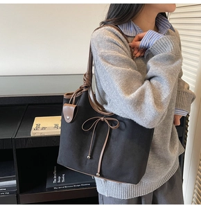 Detail of black tote bag with brown leather bow and trim worn on the shoulder