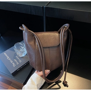 Macro view of textured brown leather bucket bag with flap closure on a modern shelf