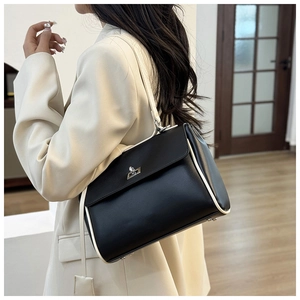 Detail of a black leather bucket bag with white piping and silver clasp worn by a model