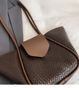 Close-up of deep brown woven tote bag with a golden metal buckle on a neutral background