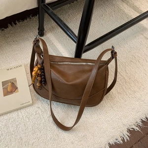 Brown leather shoulder bag with zipper and wooden bead charm on a plush white rug