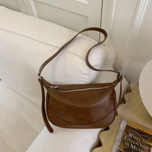 Elegant brown leather hobo bag with adjustable strap displayed on a white sofa