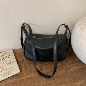 Minimalist black crescent shoulder bag with zipper on a wooden surface with magazines
