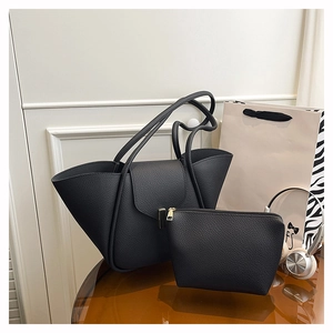 Detail of black lychee grain leather tote bag with matching inner pouch on a glass table