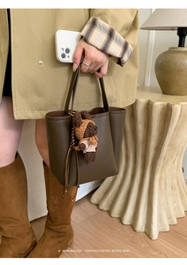 Detail of dark brown leather bucket bag with a cute knitted bear charm for daily commute