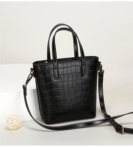 Detail of crocodile embossed leather texture and brass hardware on black bucket bag
