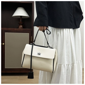 Detail of minimalist cream bucket bag featuring black edge trim and silver twist lock