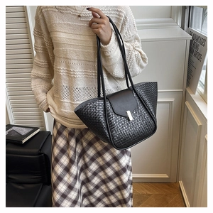 Detail of black woven tote bag featuring leather flap and silver metal lock closure