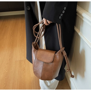 Detail of a brown retro bucket bag with drawstring strap worn by a model in a minimalist setting