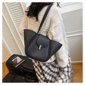 Detail view of black lychee grain leather shoulder bag with gold metal clasp on a model