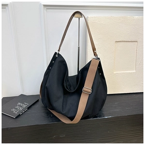 Detail of black canvas hobo bag featuring brown leather handle and wide crossbody strap