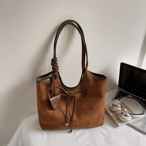 Brown suede tote bag with bow detail and leather handles in minimalist office setting