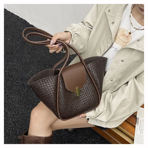 Detail of dark brown woven tote bag with smooth leather flap and gold buckle closure