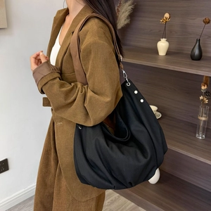 Detail of large black canvas tote bag with brown nylon strap on model in corduroy jacket