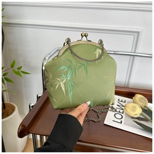 Détail d'un sac en soie verte avec broderie de bambou dorée et poignée en métal bronze