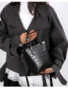 Detail showing crocodile pattern texture and bronze hardware on black bucket bag